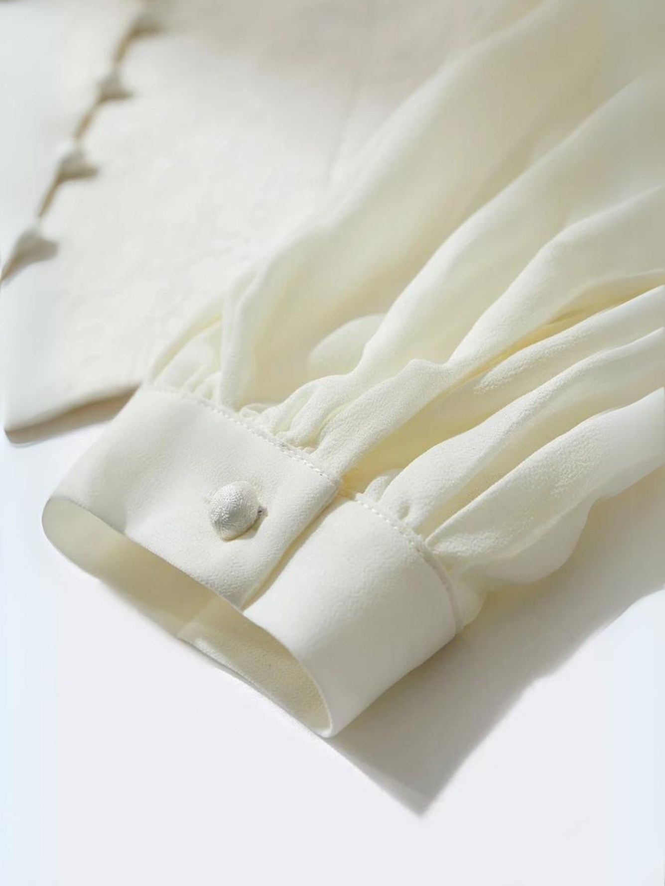 Fabric detail of cream blouse showing buttoned cuffs and texture
