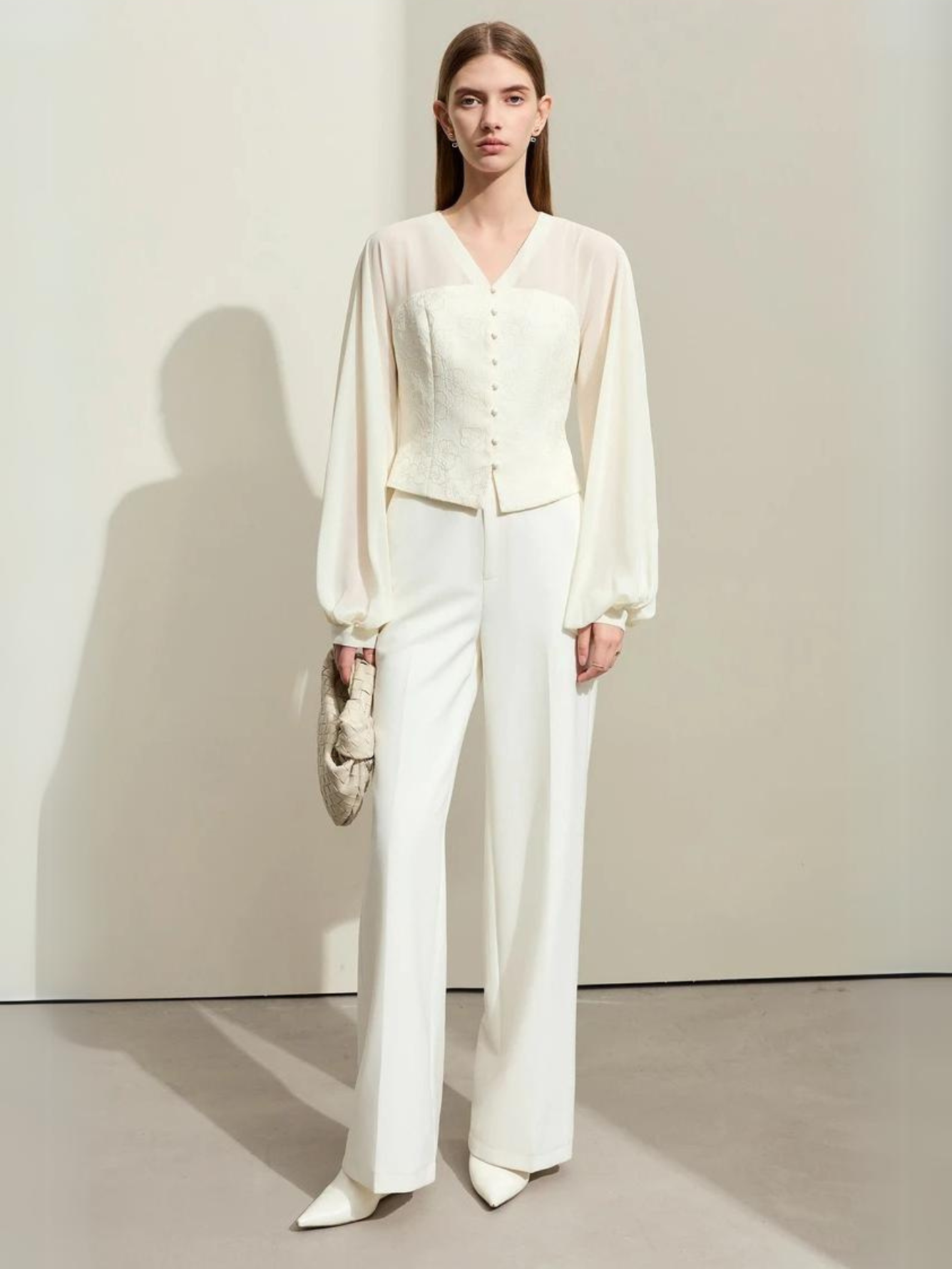 Model walking in cream blouse and white trousers
