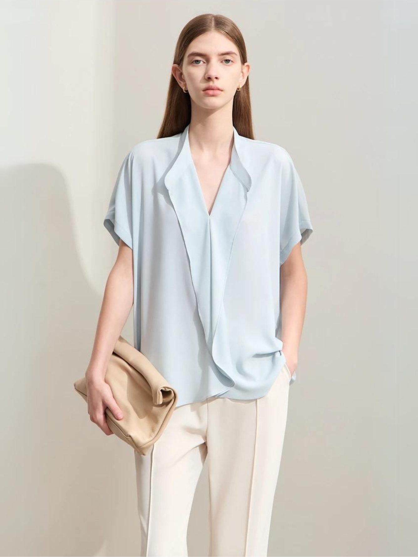Light blue blouse with V-neck and soft drape, styled with a clutch