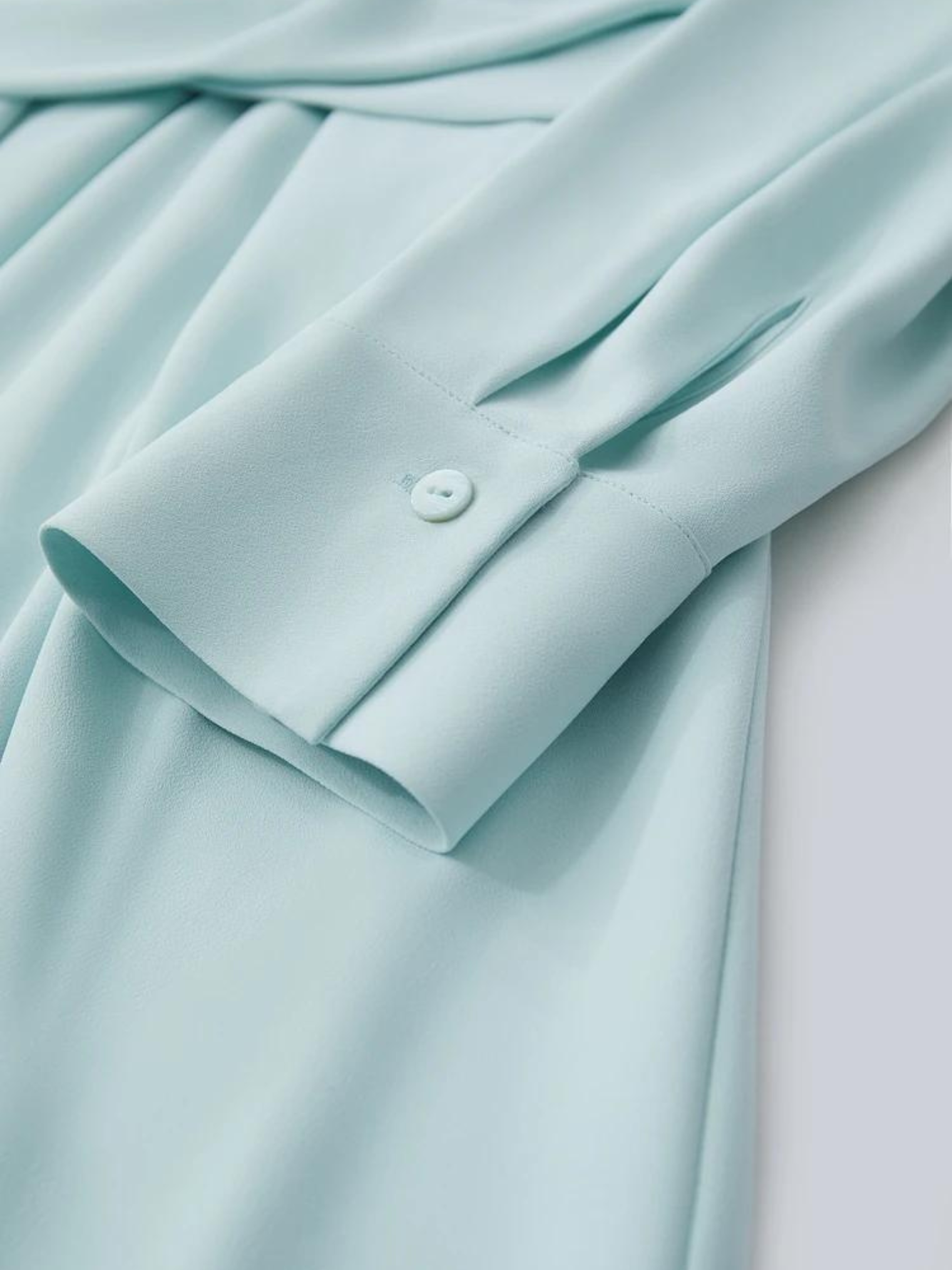 Close up of a baby blue dress with long sleeves focusing on the button design on the cuffs of the sleeve.