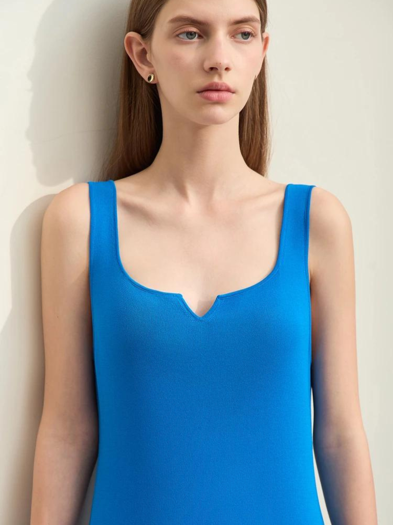 A woman wearing a blue, sleeveless dress with thin straps and a small cut out in the neckline.