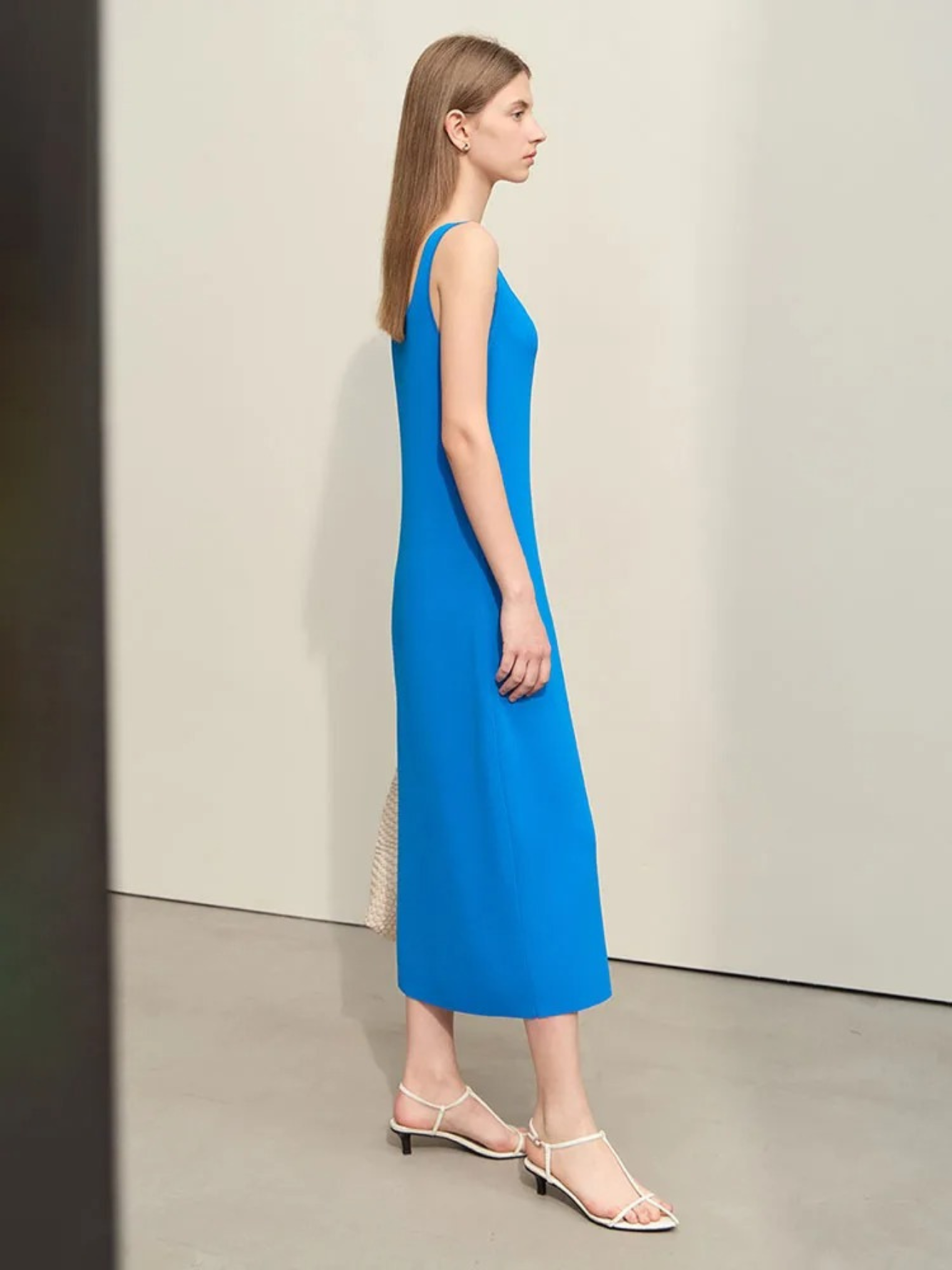 A woman wearing a minimalist, blue, mid-calf length dress with thin straps paired with simple open toed sandals,