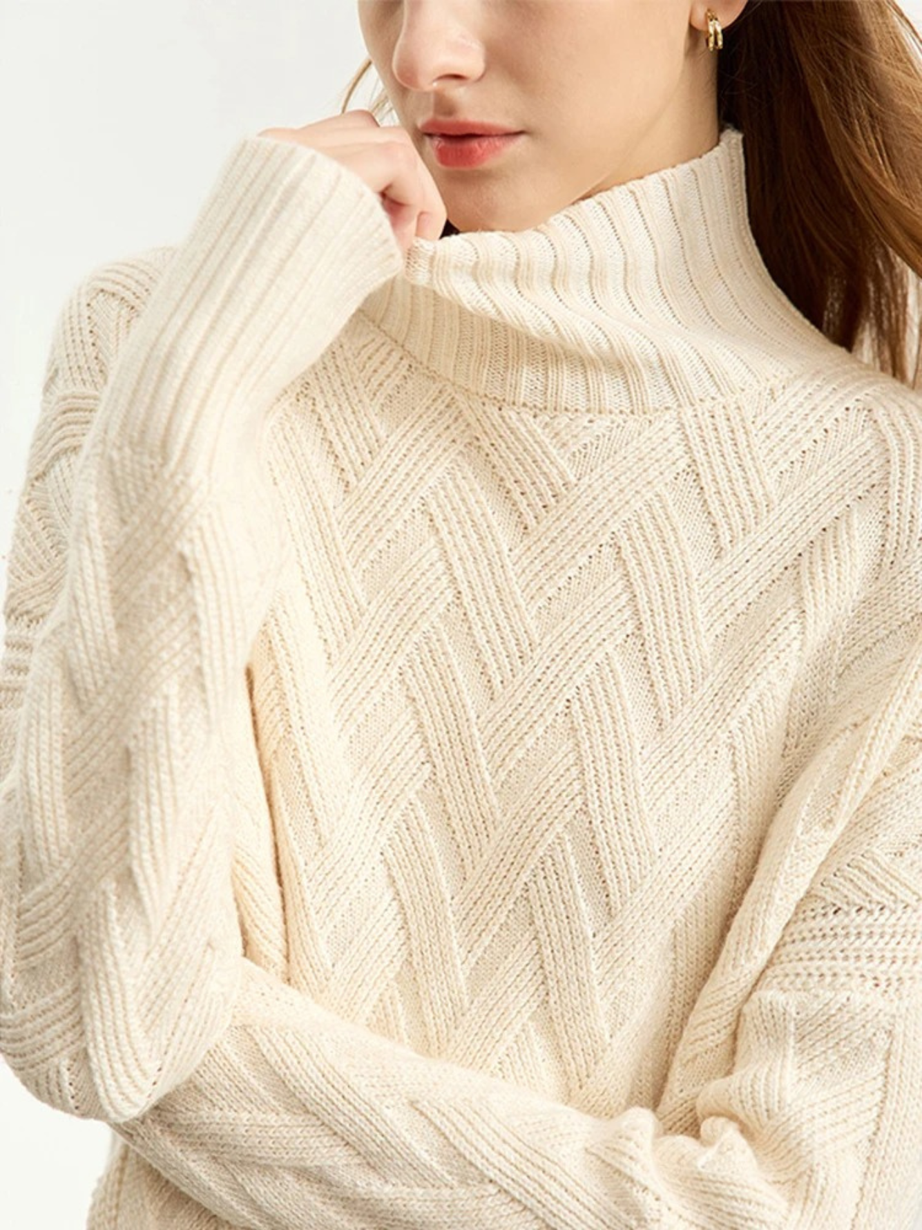 A close up of a cream colored turtleneck sweater with a ribbed design on the neckline and wrists and a chevron knit pattern.