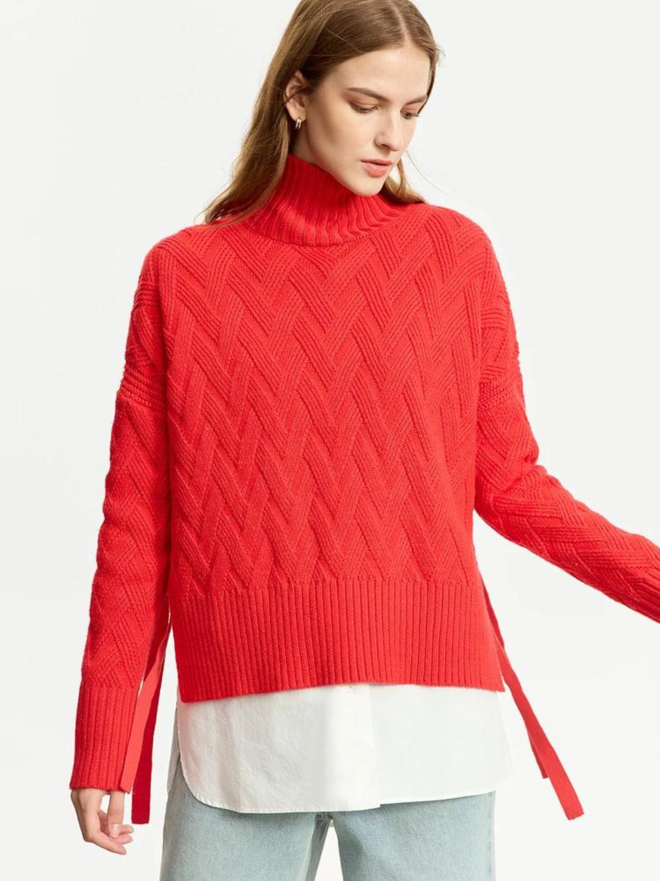 A woman wearing a red knit sweater with a turtleneck neckline and tie design on the sides over a white shirt.