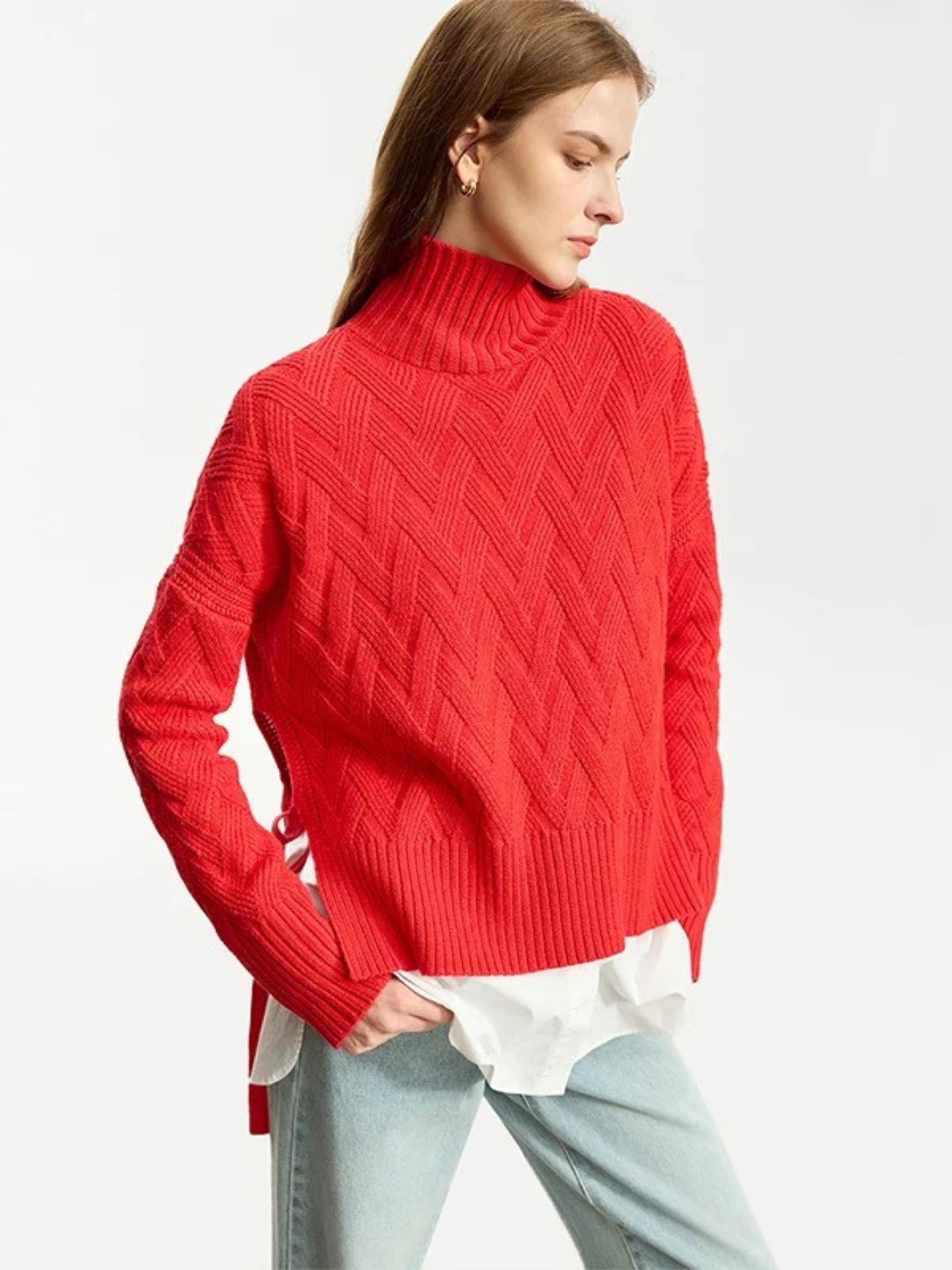 A woman wearing a red knit sweater with a turtleneck neckline and tie design on the sides over a white shirt.