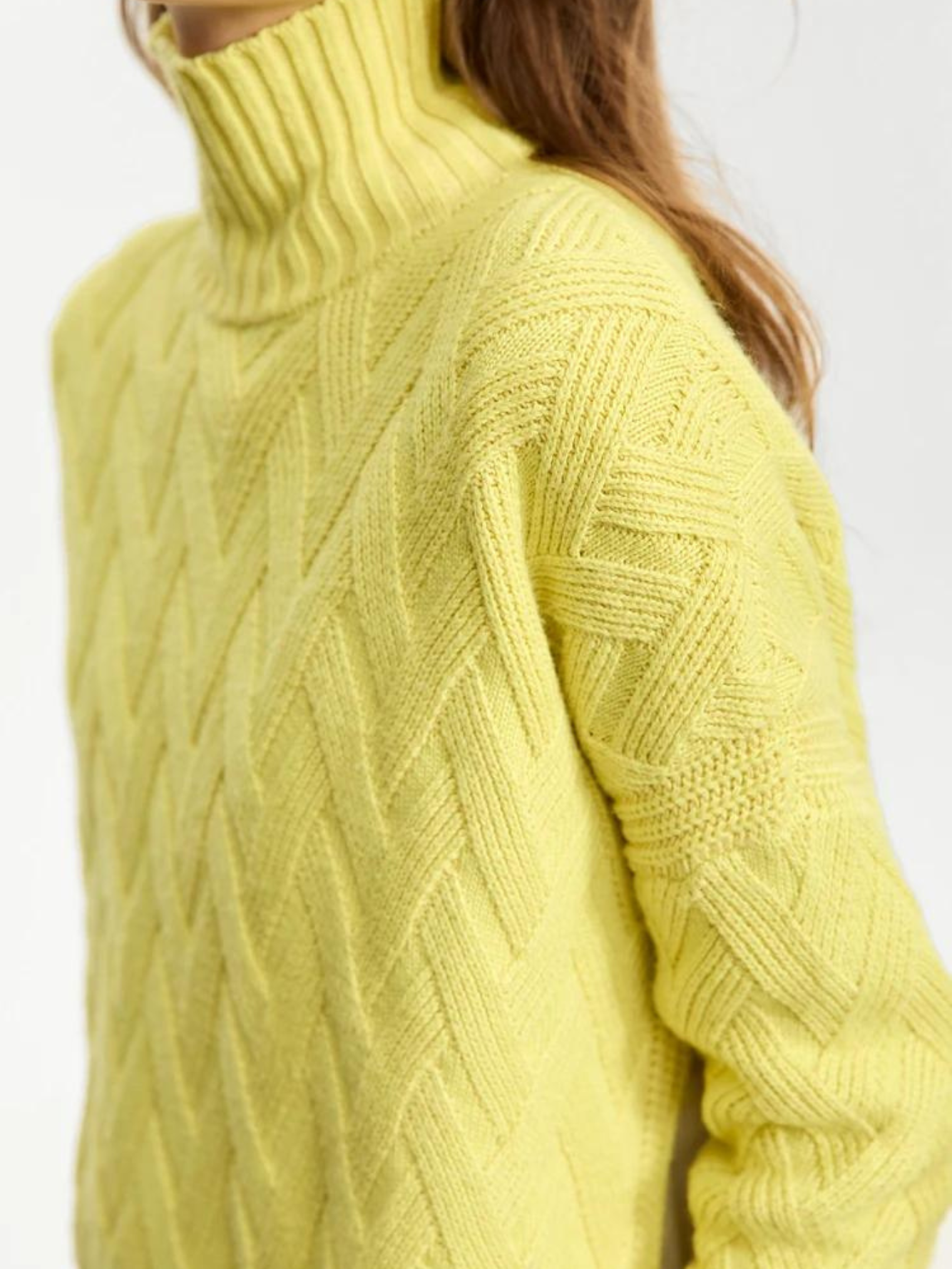 A close up of a mustard colored knit turtleneck sweater with a chevron knitting pattern.