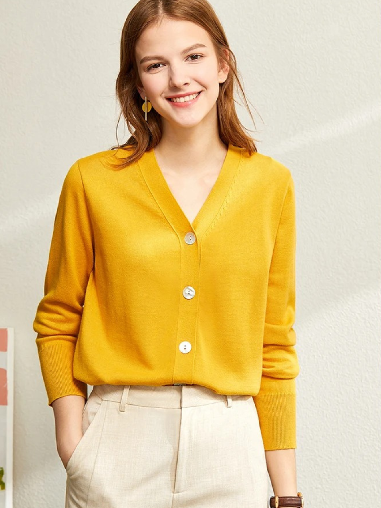 Woman in yellow cardigan smiling with hand near face