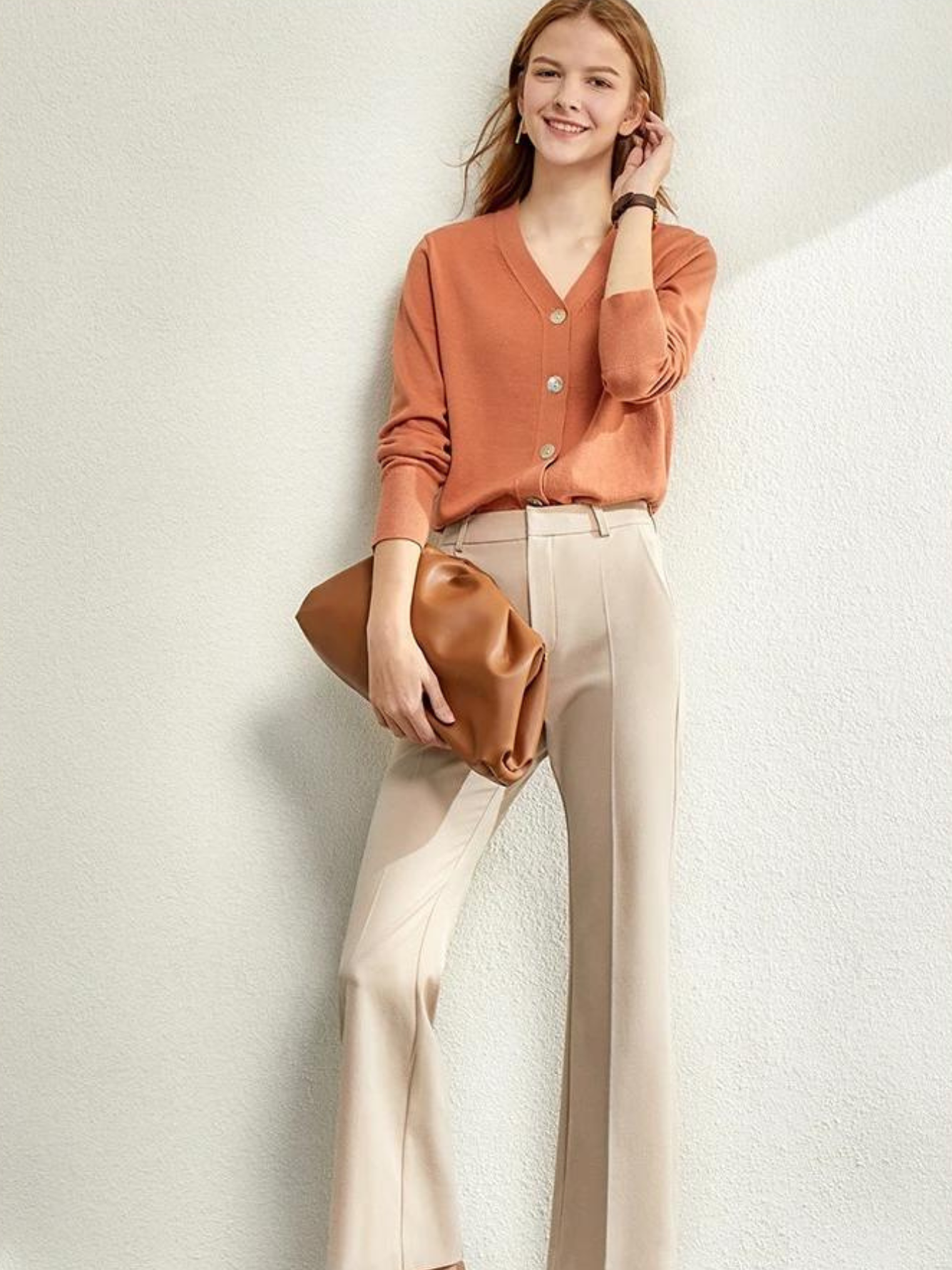 Model seated wearing rust cardigan and cream wide-leg pants

