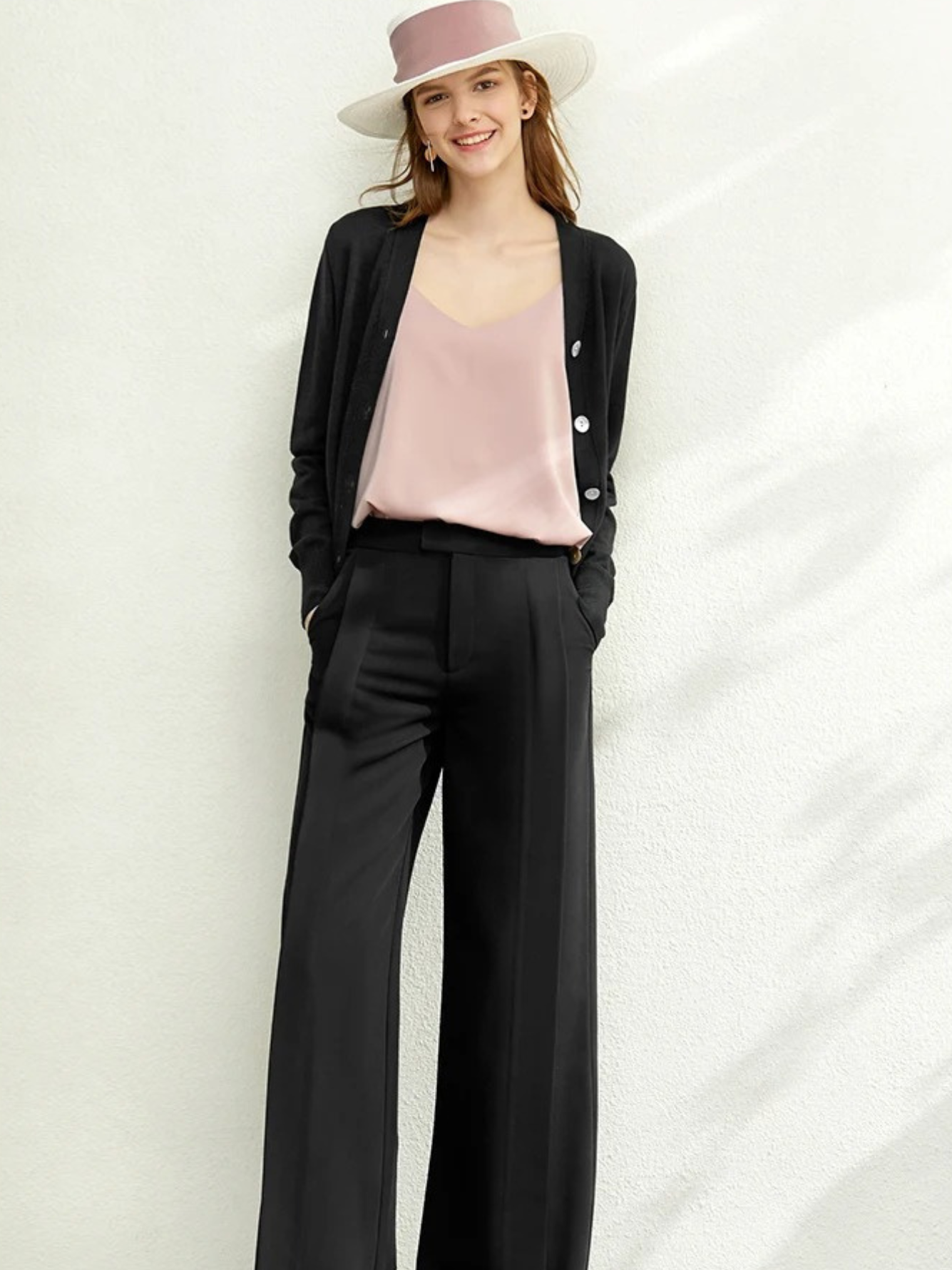 Woman in black cardigan over pink top and black trousers with hat

