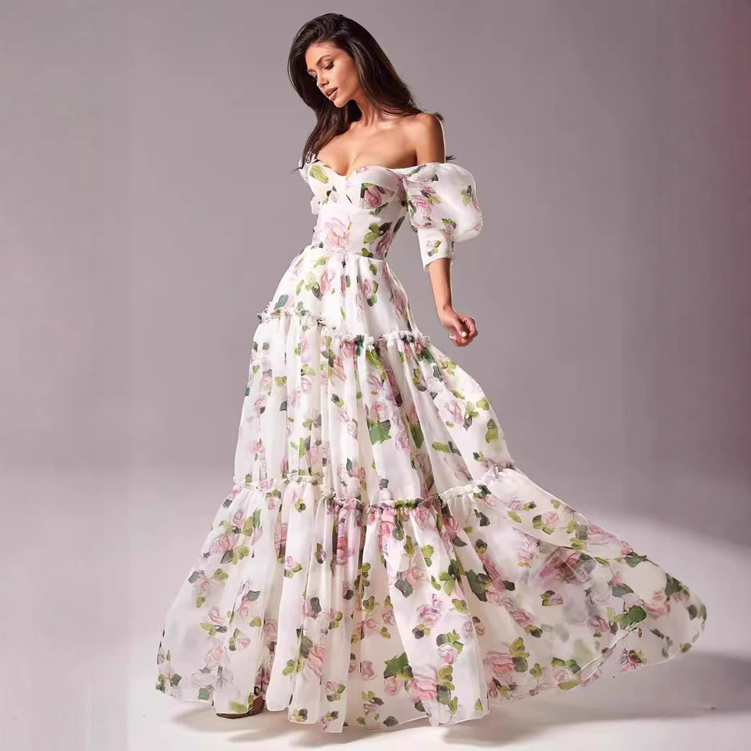 Kvinnens elegante maxikjole med avskåret skuldre, volangermiddels og blomsteracenter