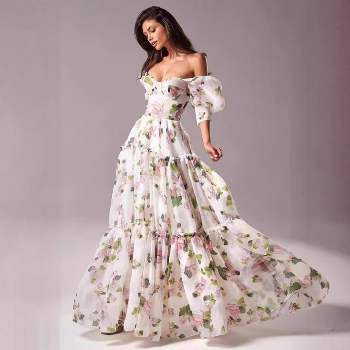Kvinnens elegante maxikjole med avskåret skuldre, volangermiddels og blomsteracenter