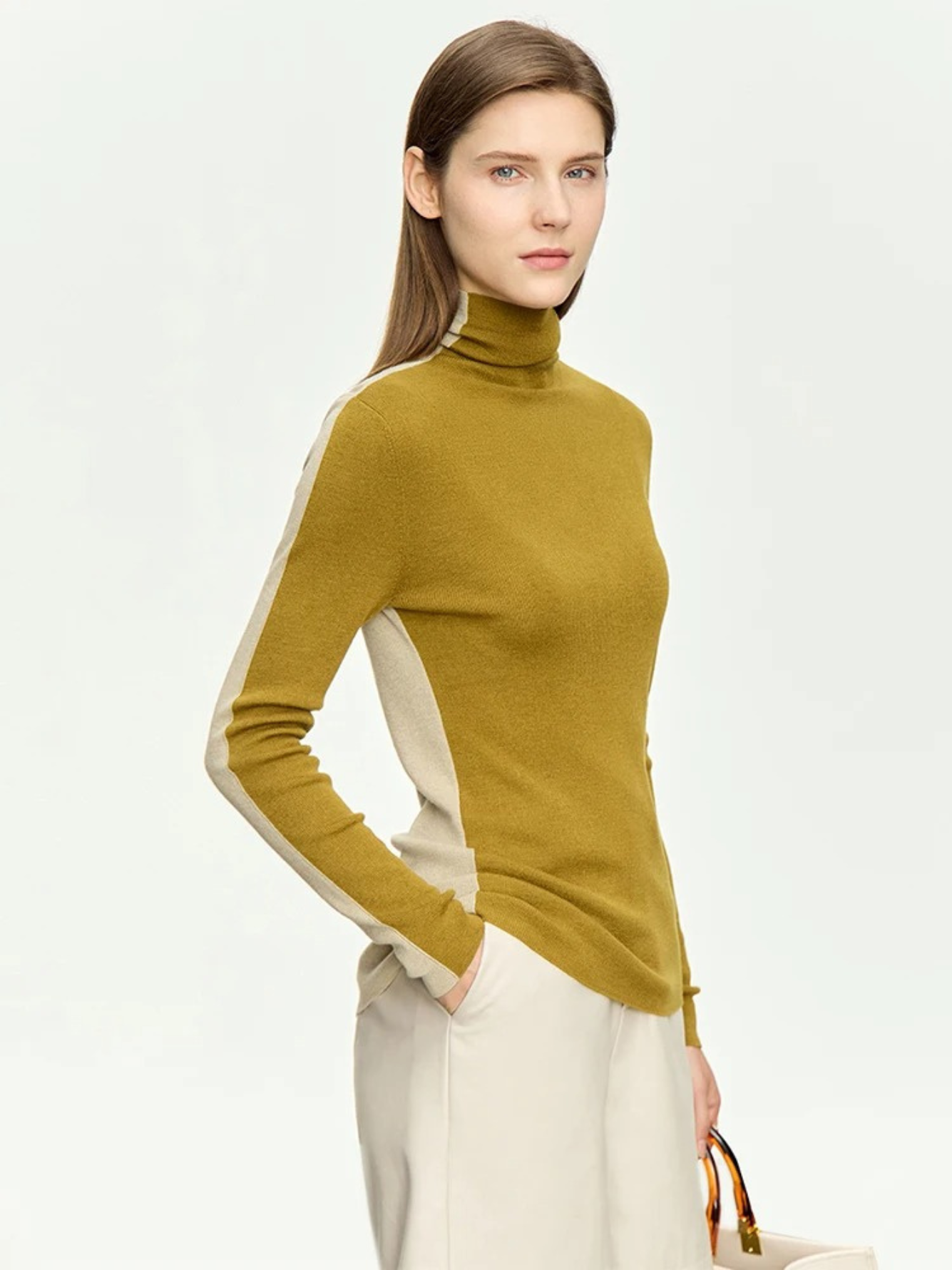 A woman wearing a dual toned turtleneck sweater featuring a mustard yellow color in the front and a pale yellow color in the back.