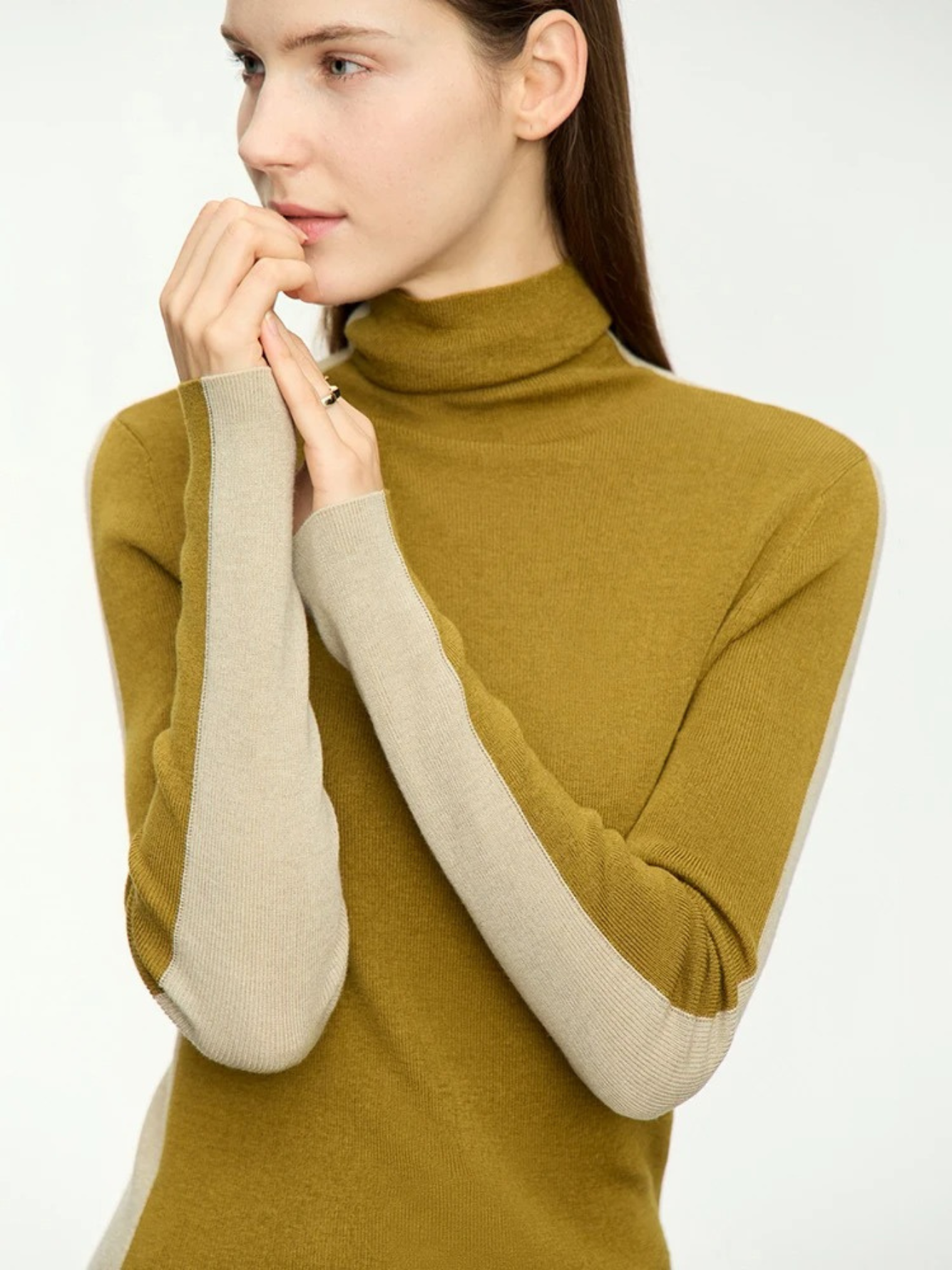 A woman wearing a dual toned turtleneck sweater featuring a mustard yellow color in the front and a pale yellow color in the back.