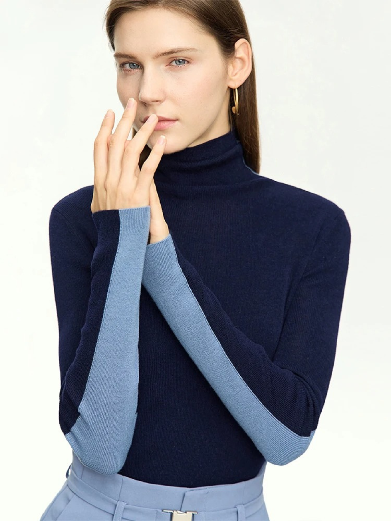A woman wearing a dual toned dark blue and light blue turtleneck sweater that is interchangeable to achieve two looks.