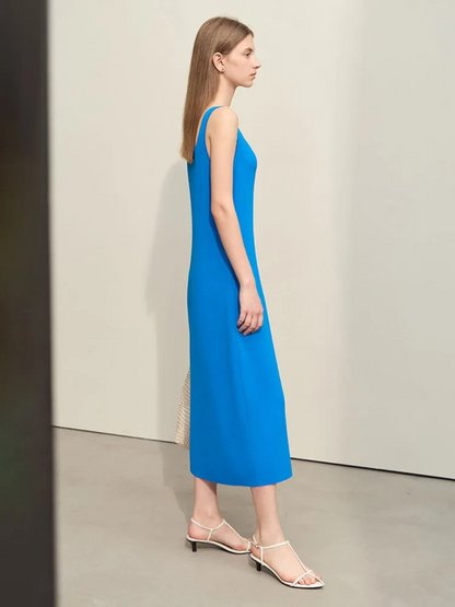 A woman wearing a minimalist, blue, mid-calf length dress with thin straps paired with simple open toed sandals,