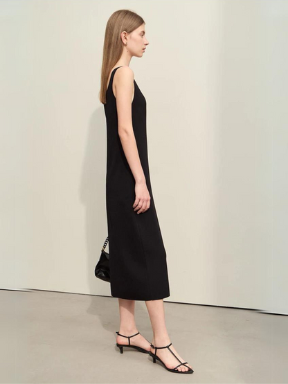 A woman wearing a minimalist, knee length, sleeveless dresses with thin straps and a mini cut out in the neckline in black.