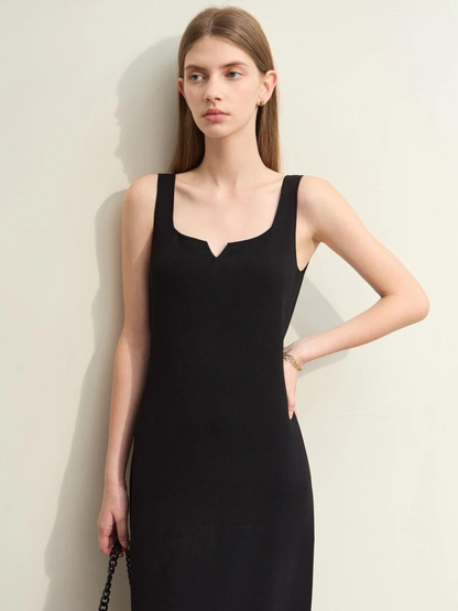 A woman wearing a minimalist, knee length, sleeveless dresses with thin straps and a mini cut out in the neckline in black.